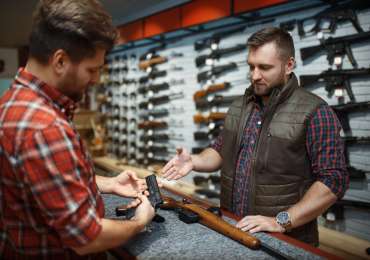 Man with owner choosing handgun in gun shop